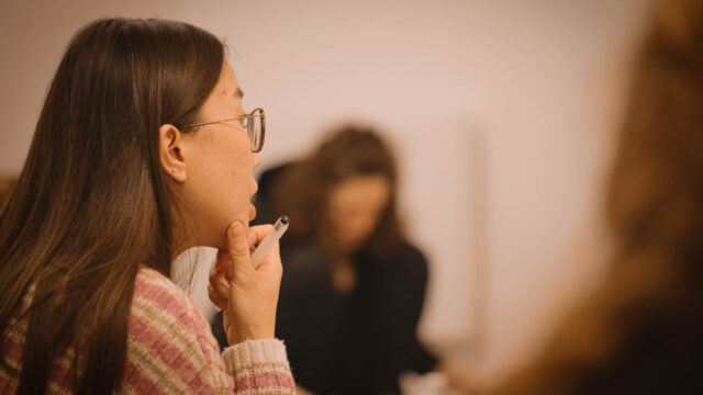 Close-up d'un visage vue de 3/4 de derrière d'une élève écoutant attentivement, tenant un stylo à la main, avec un effet de flou artistique pendant la formation de Yin Yoga Paris 15