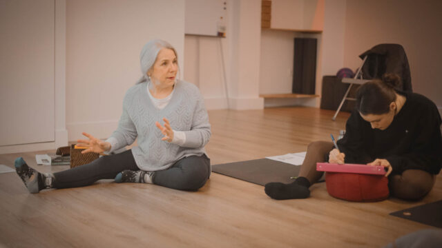 Isabel, professeur de Hatha, Yin Yoga et Yoga prénatal expliquant aux élèves tandis qu'une élève prend des notes pendant une session de formation 200h de Yin Yoga à Paris 15.