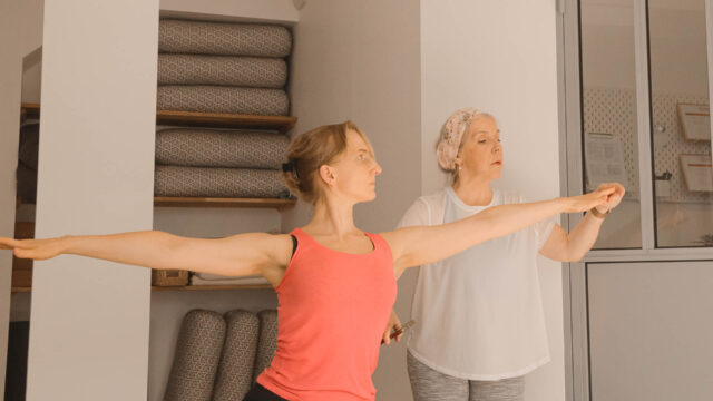 Isabel ajuste le bras d’une élève en posture de Guerrier 2 pendant la formation 200h Hatha Yoga au studio du XVe arrondissement de Paris.