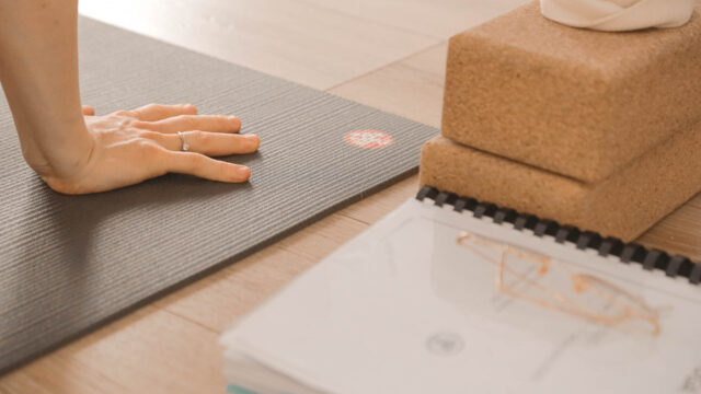 Main posée sur un tapis Manduka à côté du manuel d’anatomie et de briques en liège pendant la formation 200h Hatha Yoga au studio du XVe arrondissement de Paris.